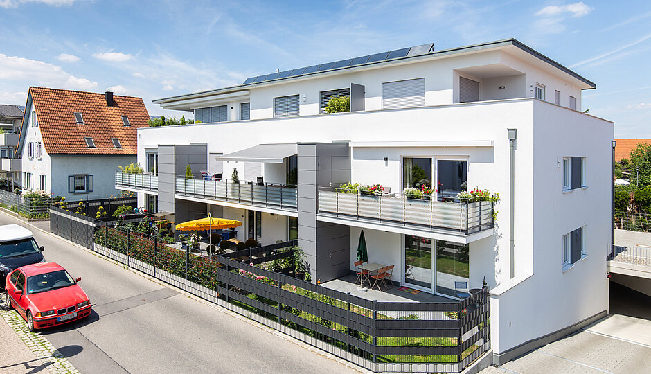 Ein Wohnhaus mit Balkons, Gärten und geparkten Autos