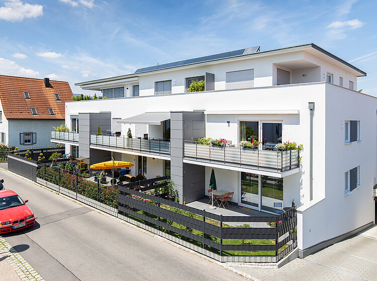 Ein Wohnhaus mit Balkons, Gärten und geparkten Autos