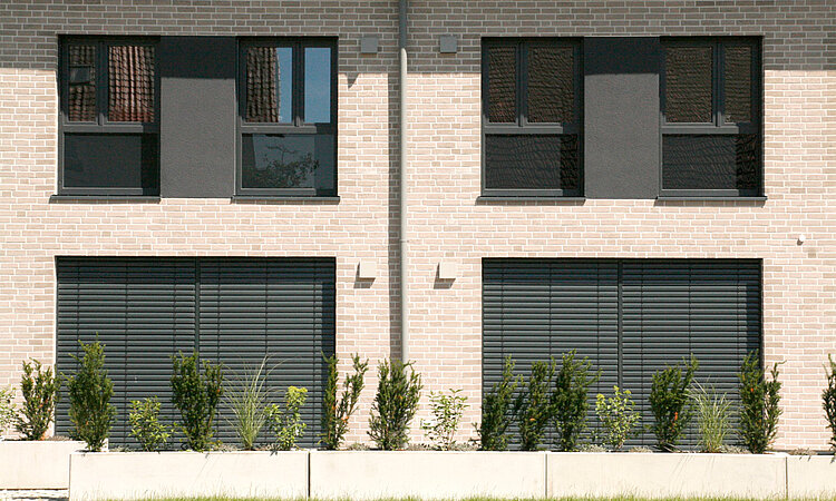 Fensterfront eines Wohnhauses mit Sträuchern und Rasen.