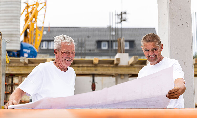 Mathis Bau Team Zwei Bauarbeiter schauen auf einer Baustelle auf einen Bauplan