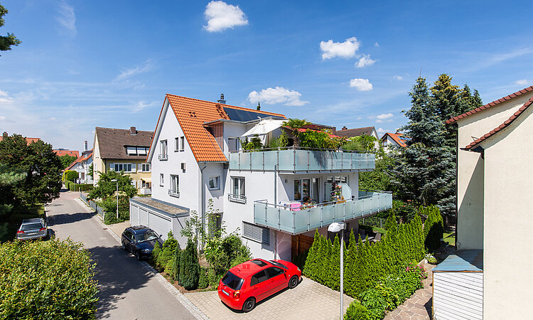 Wohnhaus mit großem Balkon und geparktem Auto an einer Straße